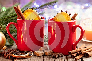 Red mugs of hot mulled wine, Christmas tree branches and garland bokeh lights on background.