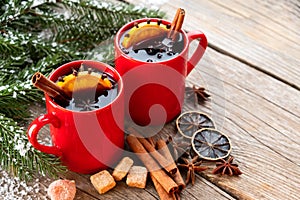 Red mugs of hot mulled wine with spices and Christmas tree branches covered with snow. Copy space for text.