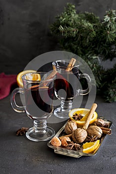 Red mulled wine in glasses at black background. Fir wreath, orange, cinnamon, nuts, cone and spices