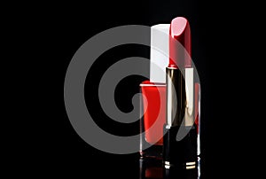 Red nail polish in bottle and scarlet lipstick on glossy black background, place for text, selective focus