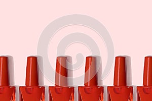 Red nail polish bottles in row on pastel pink background top view