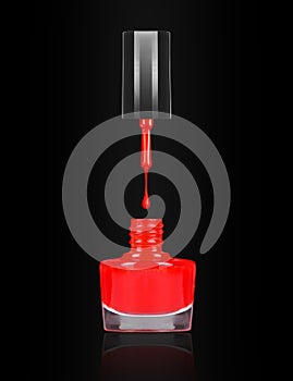 Red nail polish dripping from brush into bottle on black