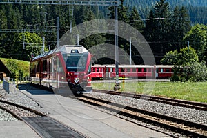 Red narrow gauge train arrives at a remote train station in the Swiss Alps