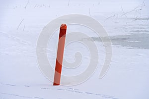 Red navigational spar buoy on a frozen lake