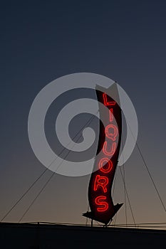 A red neon liquors store sign glowing during a sunset