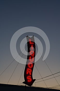 A red neon liquors store sign glowing during a sunset