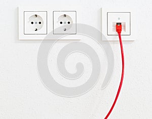 Red network cable in wall outlet for office or private home lan ethernet connection with power outlets flat view on white plaster