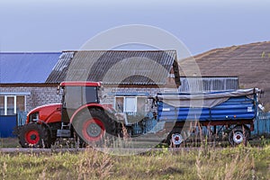 Red new wheeled tractor of medium size with blue trailer.