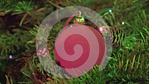 Red New Year`s ball against the background of the decorated garland of a Christmas tree