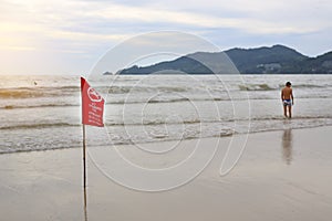 Red no swimming sign flag at beach against blur image of man on the seacoast