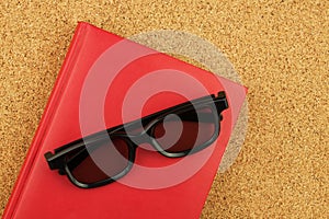 Red notebook and black glases on the cork board