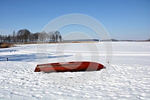 Red old boat on snowy winter lake coast