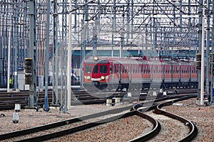 The red old electric train arrives at the station of the railway station Track, poles and supports for current-carrying lines