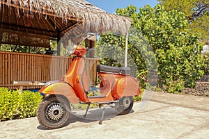 Red old-fashioned scooter motorbike - indonesian traditional way of transportation on a tropical island. Orange vintage vespa.