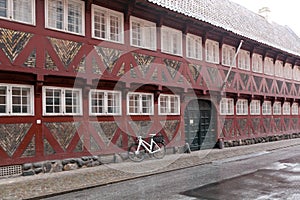 Red old house with white windows - half-timbered house made of wood and bricks. Bicycle near the wall