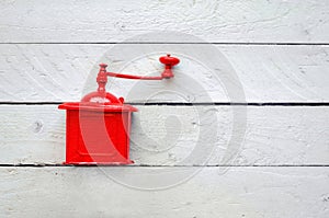 Red old vintage mechanical coffee grinder on white wooden table.