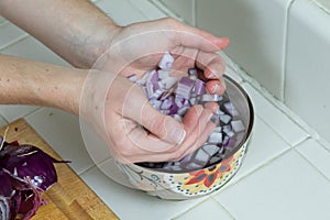 Red onions being dropped into a small bowl of water