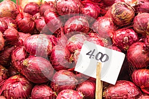 Red onions fresh and organic on sale at a vegetable stand in a food local market with the white price tag right side on wood stick