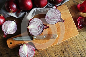 Red onions on wooden chopping cutting board on textile napkin over dark wooden rustic texture background. Top view