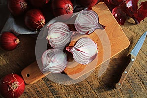 Red onions on wooden chopping cutting board on textile napkin over dark wooden rustic texture background. Top view