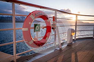 Red orange AIDA Bella lifebuoy attached to the cruise ship railing, sunset above Iceland snow mountain range in the background,