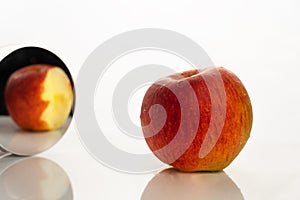 Red orange apple fruit for food in the mirror in paradox reality concept on white background