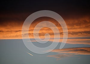 Red and orange clouds at sunset with jet aircraft vapour trail