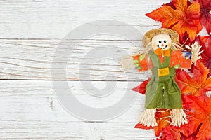 Red and orange fall leaves with a scarecrow on weathered whitewash wood textured background photo
