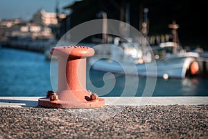 A red orange mooring bollard with a fishing boat in the background