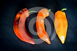 Red, Orange and yellow organic sweet pointed peppers on a blackboard, natural light