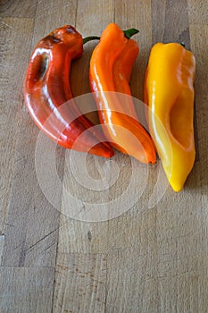 Red, Orange and yellow sweet pointed peppers on a wooden cutting board