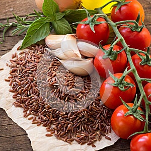 Red organic rice, tomatoes, olive oil, garlic and herbs on wood