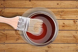 Red paint can with brush on wooden floor