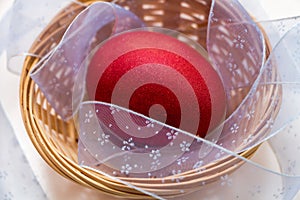 A red painted Easter egg lies in a wicker basket