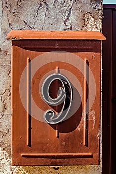 Red painted steel mail box with number nine on concreat fence