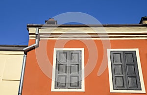 Red painted wall with two windows and closed shutters under blue sky in historic part of Lviv, Ukraine