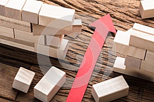 Red Paper Arrow Amidst Blocks On Wooden Table