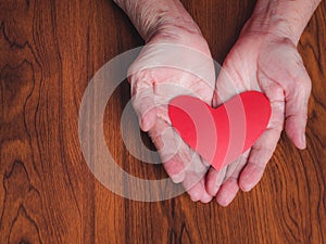 Red paper cut a heart shape on the palm of a senior woman. Valentine`s day. Close-up photo. Concept of aged people and love