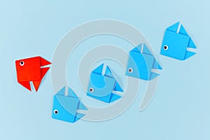 Red paper fish changing direction while swimming ahead of line of blue fish Concept for new business strategies and change