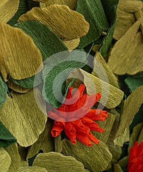 Red paper flower among green leaves, origami