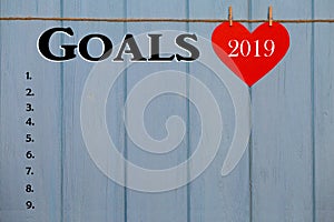 Red paper heart with 2019 goals list on blue wooden background, banner with copy space for text