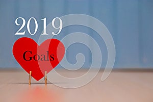 Red paper heart with 2019 goals list on blue wooden background, banner with copy space for text