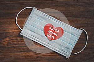 Red paper heart with #STOP ASIAN HATE text on surgical face mask with dark wood background photo
