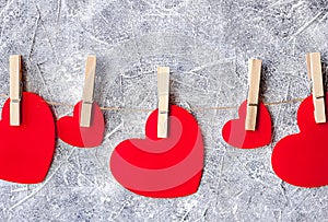 Red paper hearts hanging on linen twine rope with spins on bleack and white wall background