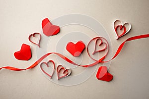 Red paper hearts and silk ribbon on gray background. Valentine`s Day absctract. Symbol of love. Copy space, flat lay