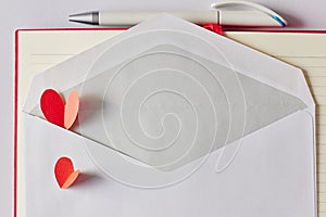 Red paper hearts in white envelope, pen and notebook