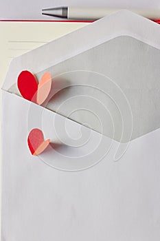 Red paper hearts in white envelope, pen and notebook