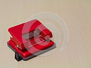 Red paper hole puncher on wooden background.