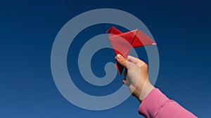 red paper origami pigeon in children& x27;s hand on blue sky background