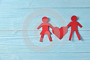 Red paper people holding heart on blue wooden background.